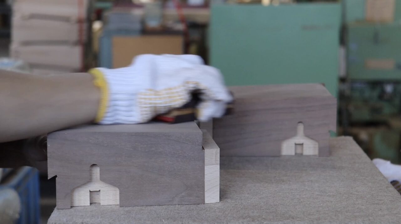 Hand finishing process: Craftsman using sandpaper to refine the surface of veneer.