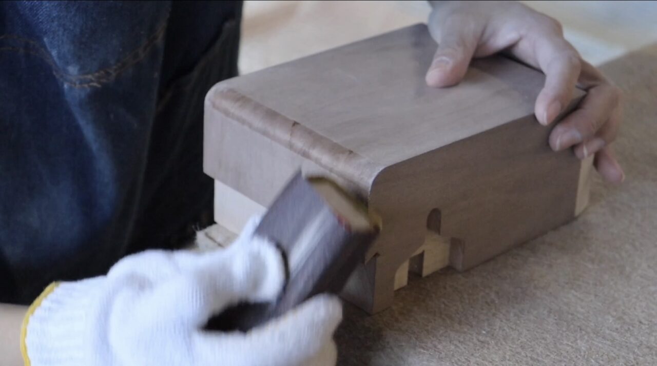 Hand finishing process for veneer; a craftsman smoothing the surface of the veneer with sandpaper.