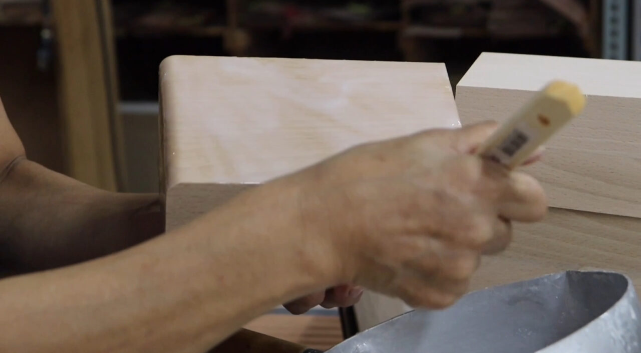 "Application of adhesive to the surface of a product to ensure even coverage, as part of the veneer bonding process.