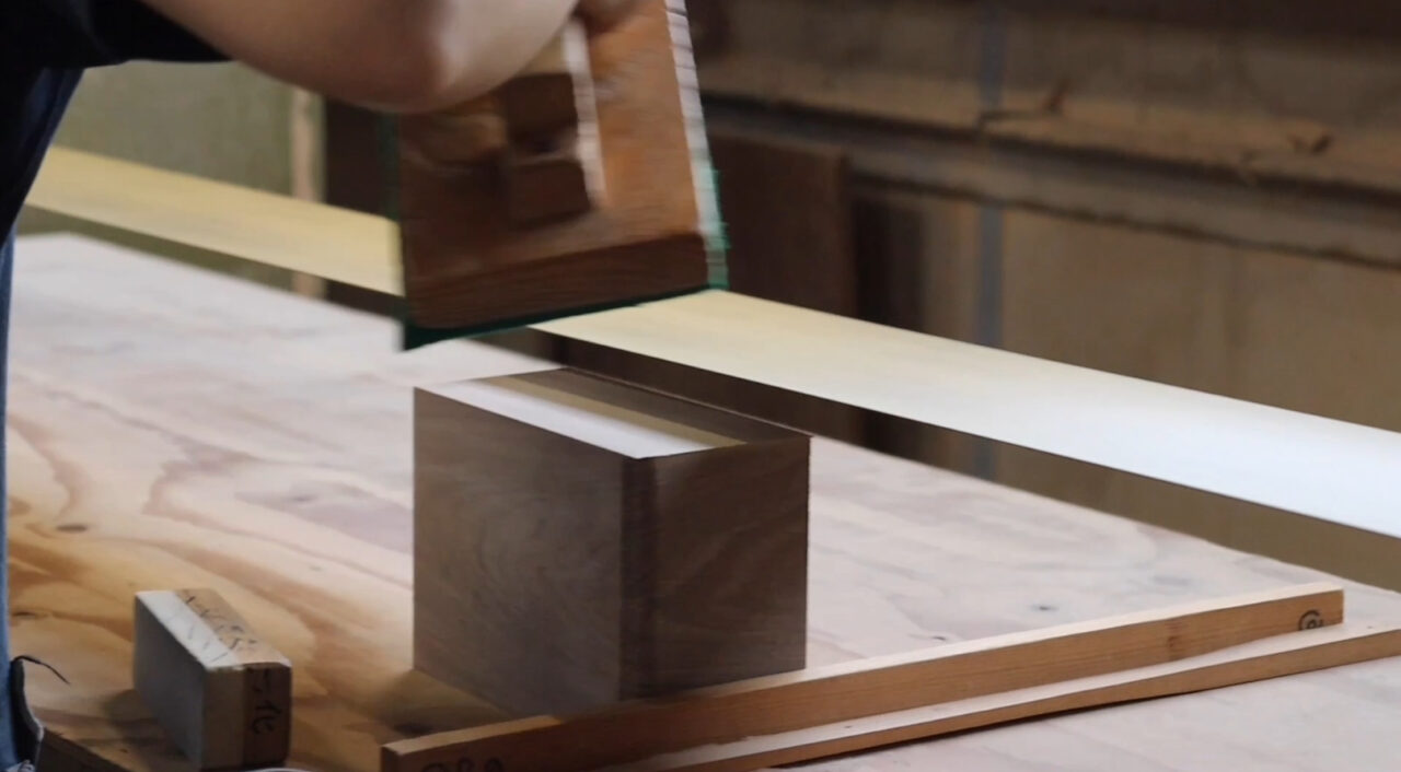 Wood sanding process using a belt sander to reveal the grain pattern. The image shows a craftsman smoothing the surface of veneer during the finishing process.
