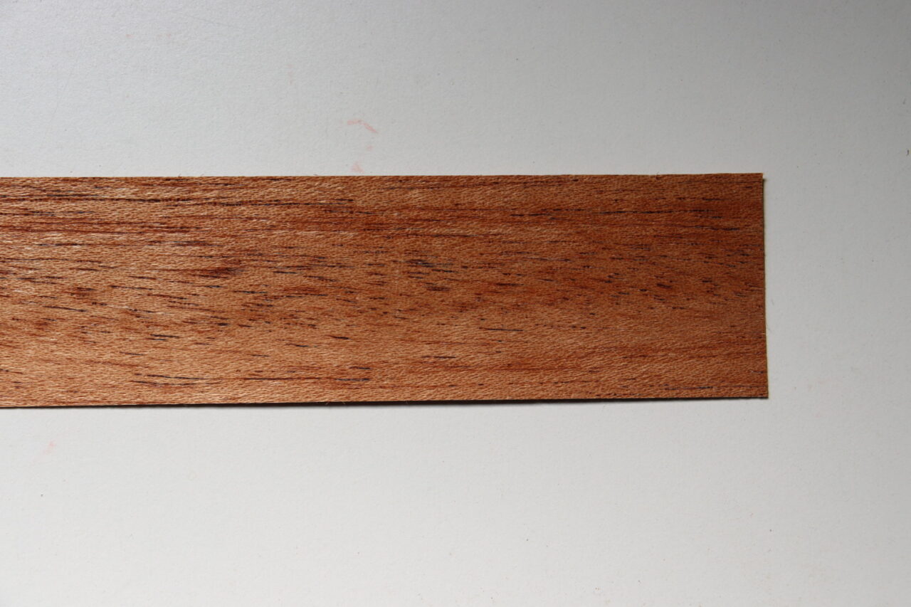 "Close-up of Sapele veneer showing distinct ribbon-like stripes and reddish wood grain, used for exterior and interior materials, as well as musical instruments