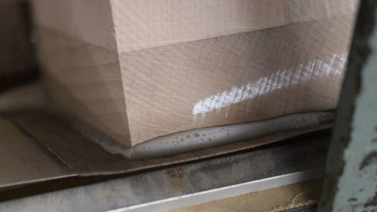 Veneer heat pressure bonding process: Image showing the veneer being fixed in a jig and heated to remove excess adhesive and achieve a smooth, uniform surface.