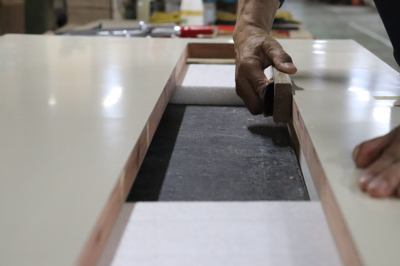 木工職人が鉋を使い、フラッシュ戸の窓枠用に開口部を手作業で仕上げている様子
