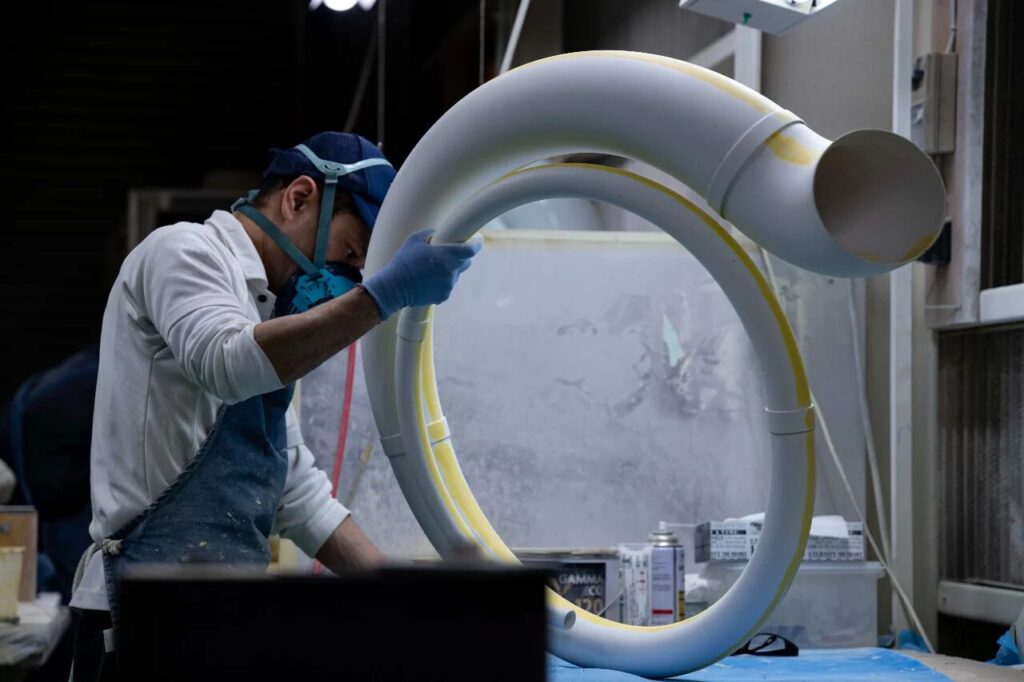 株式会社スズハルの作業員がFRP製スーザフォンの管部品にパテ作業を施している様子