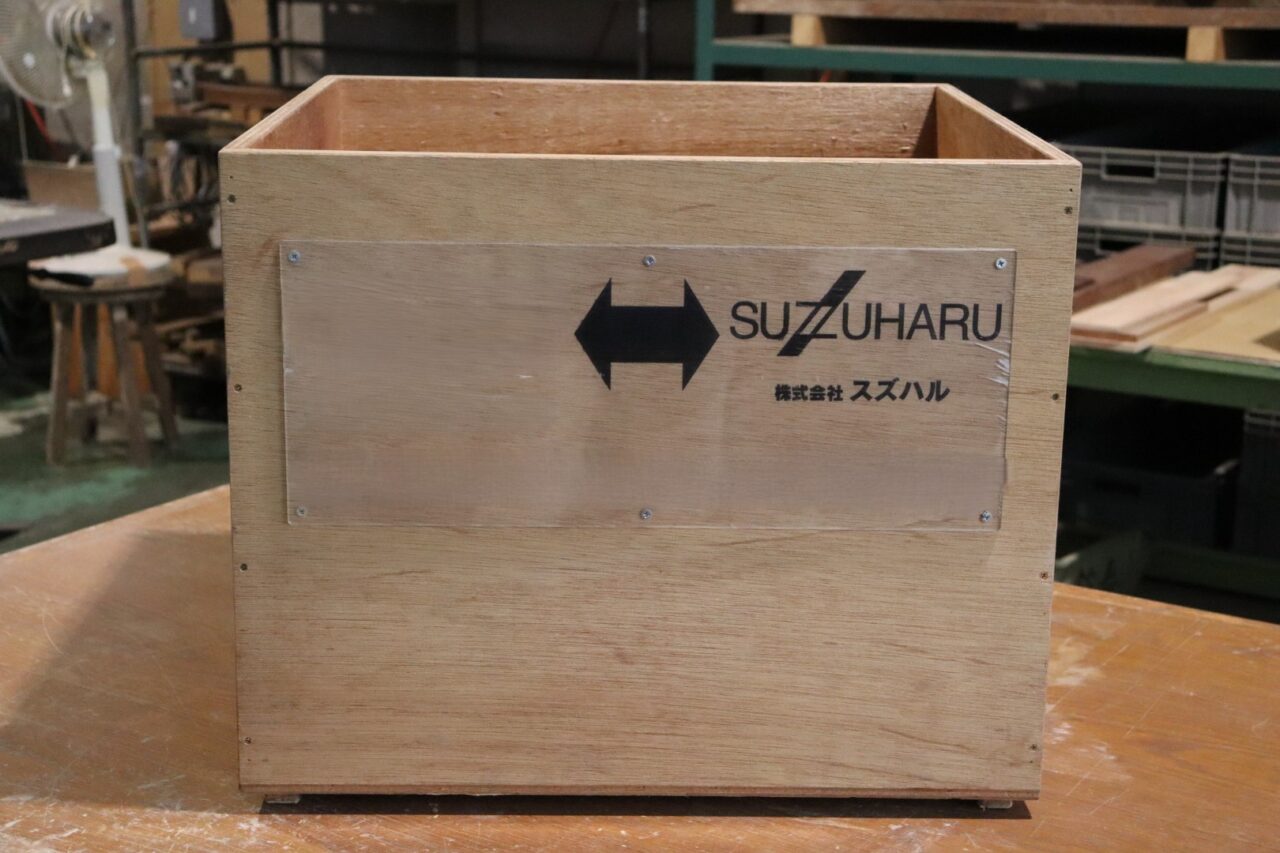 アクリル製看板が取り付けられた木製通い箱の正面画像。合板加工オーダー品のクローズアップ。