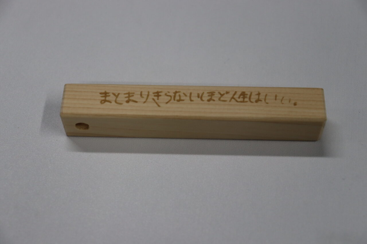 ヒノキ製の木製キーホルダーに刻まれた『まとまりきらないほど人生はいい』という言葉がデザインされたアイテム