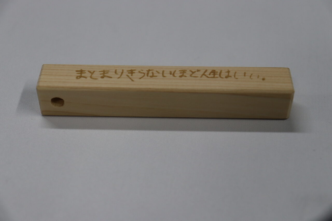 ヒノキ製の木製キーホルダーに刻まれた言葉『まとまりきらないほど人生はいい』」