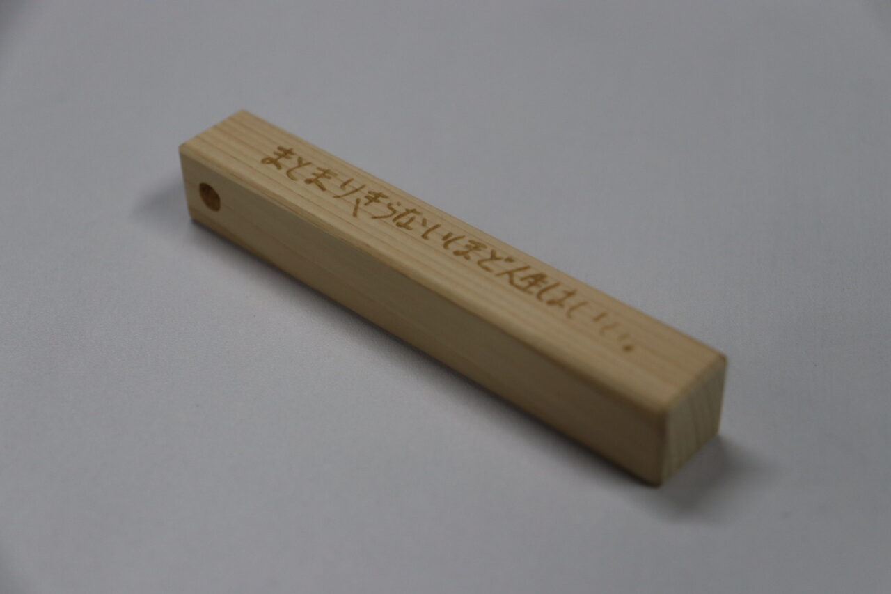 ヒノキ製の木製キーホルダーに刻まれた言葉『まとまりきらないほど人生はいい』がデザインされたアイテム