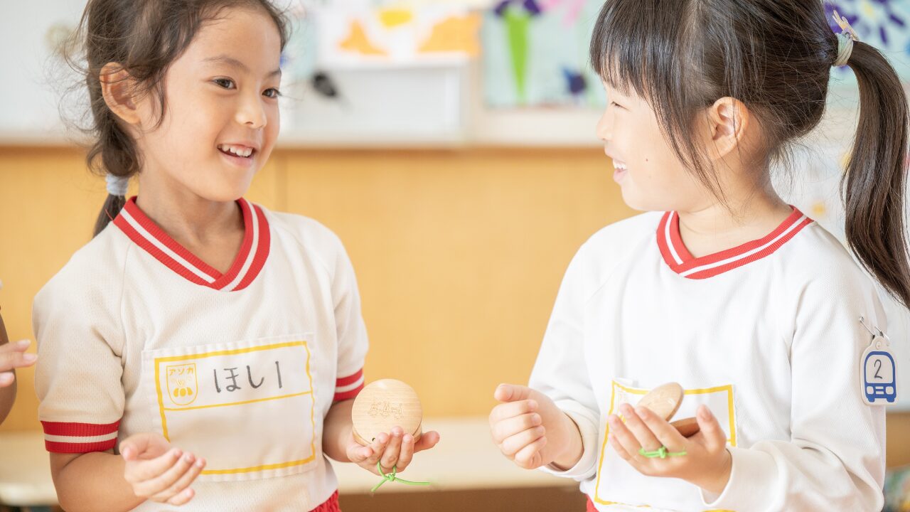 アソカ学園城北幼稚園の園児たちが向かい合い、株式会社スズハルの音育カスタネット『あそおと』を手に持ち、笑顔で演奏している様子