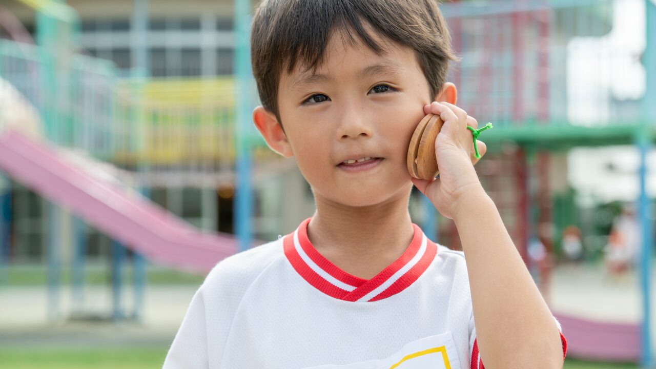 男の子の園児が、株式会社スズハルの音育カスタネット『あそおと』を頬に押し当て、楽しそうにしている正面写真
