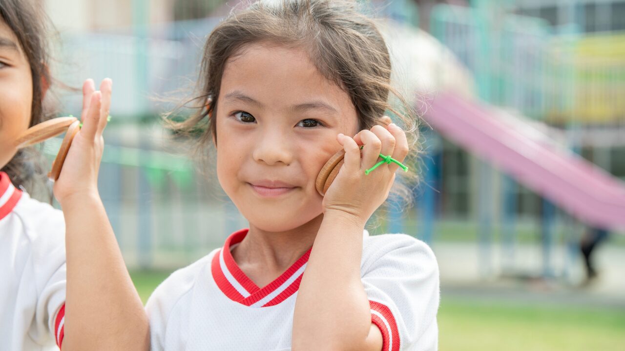 音育カスタネット『あそおと』を頬に押し当てる女園児の写真